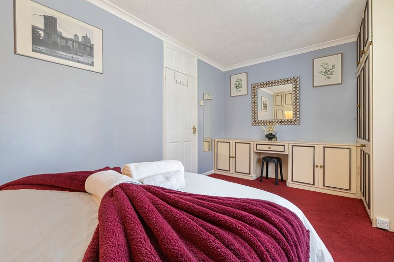 Bedroom with double bed, burgundy throw, blue walls, wooden furniture and framed artwork
