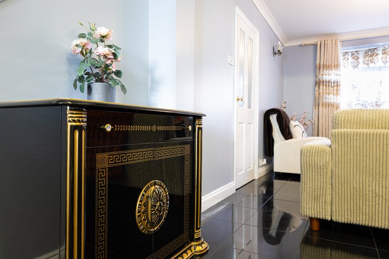 Hallway with black and gold decorative cabinet, white flowers, cream curtains and pale walls