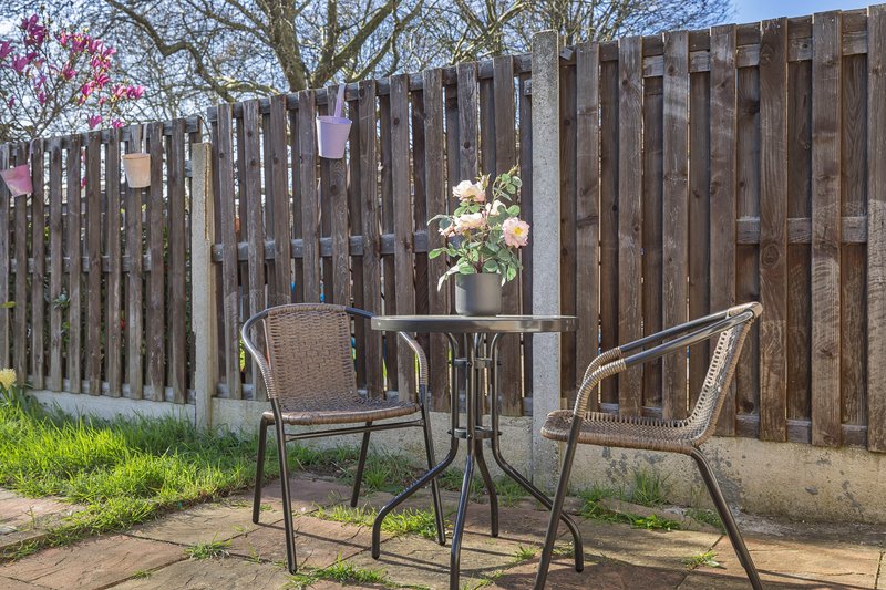 Outdoor garden seating area with two chairs, small table and potted flowers by wooden fence
