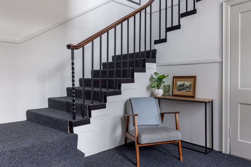 Modern staircase with black steps, wooden handrail, and mid-century chair in entryway