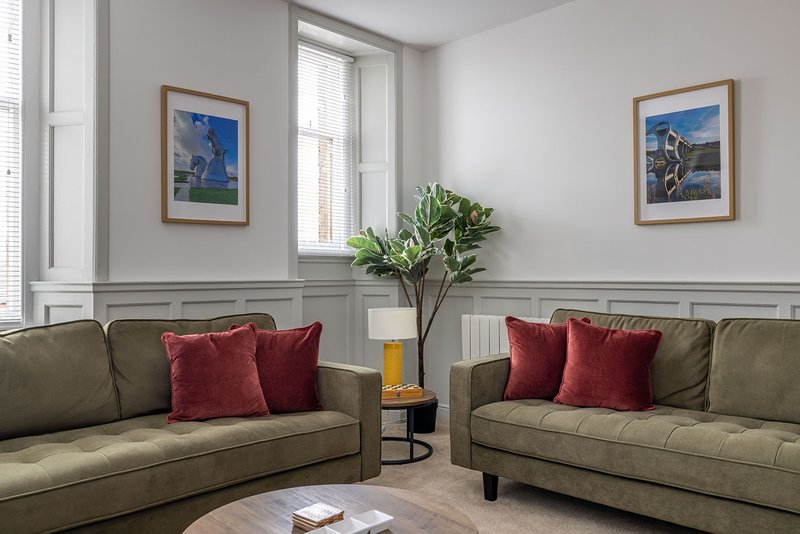 Modern living room with two olive-green sofas, red cushions, framed artwork and potted plant