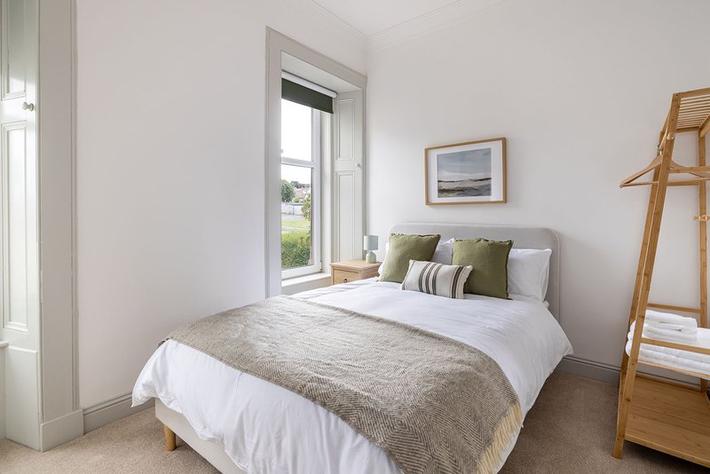 Bright bedroom with double bed, white bedding, wooden clothing rack and garden view