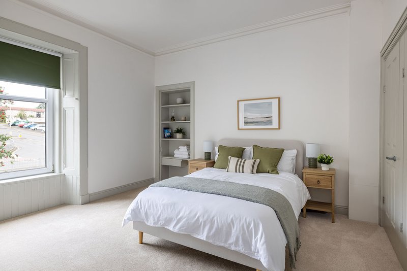 Bright bedroom with double bed, wooden nightstand, built-in shelving and window with garden view