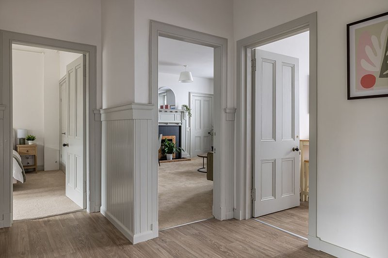 Bright hallway with multiple white doors, wooden flooring, and view into adjacent rooms