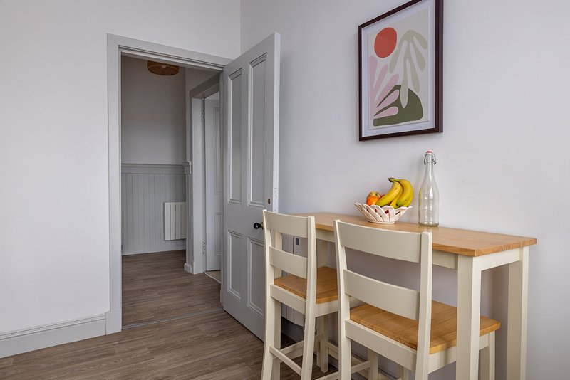 Kitchen area with wooden table, two chairs, fruit bowl, and doorway to hallway