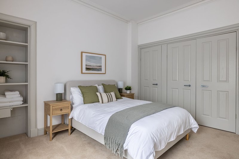 Bright bedroom with double bed, wooden nightstand, built-in shelving and fitted wardrobes