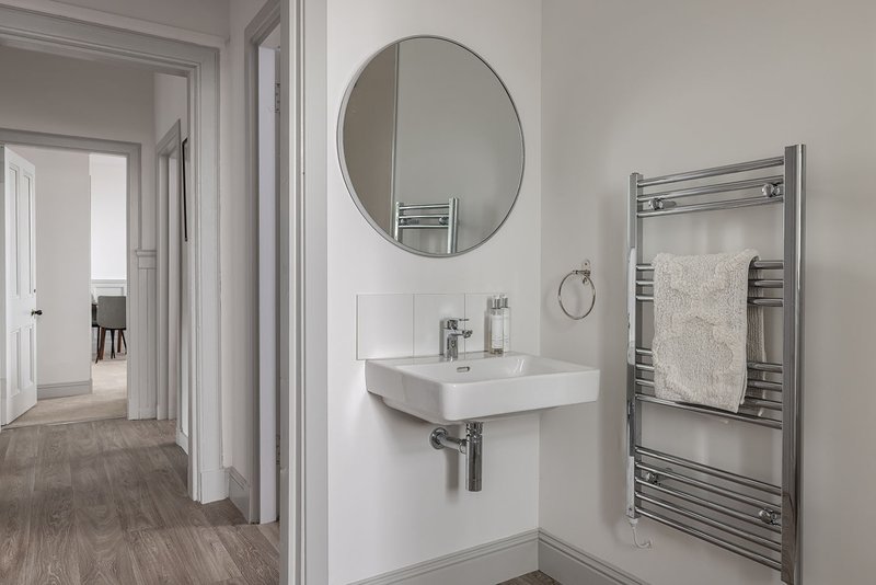 Modern bathroom with white sink, round mirror, heated towel rail and access to hallway