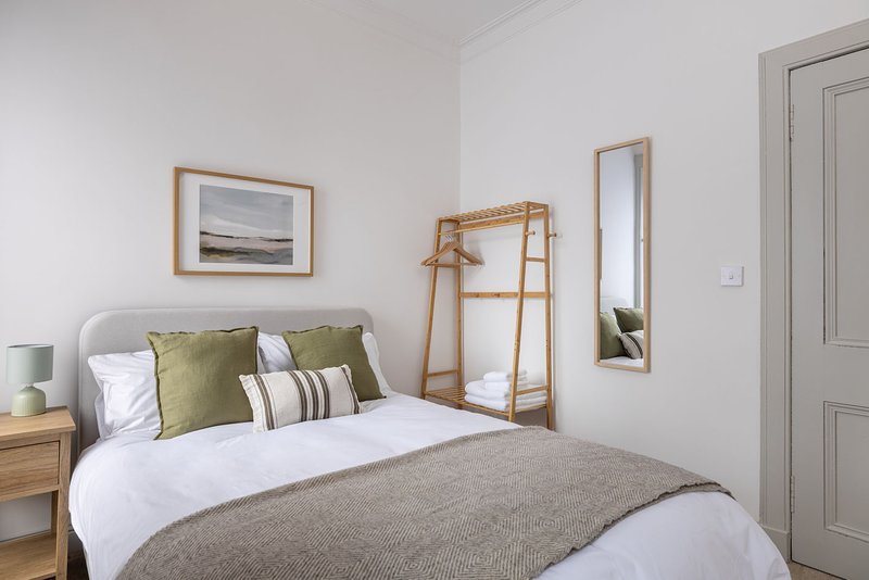 Bright bedroom with double bed, green cushions, wooden nightstand and framed artwork