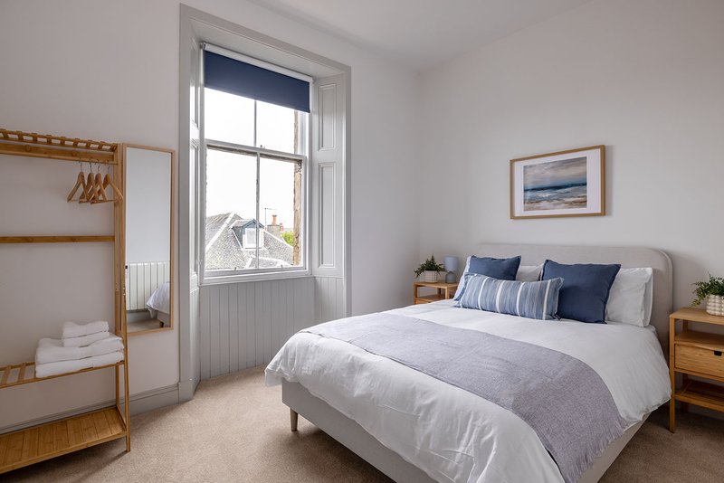 Bright bedroom with double bed, wooden furniture, window with view, and neutral décor