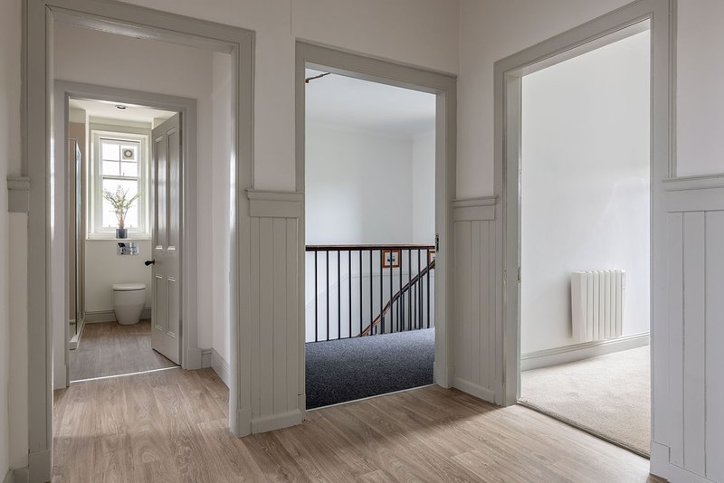 Bright hallway with wooden flooring, white panelled doors, and views to bedroom and staircase