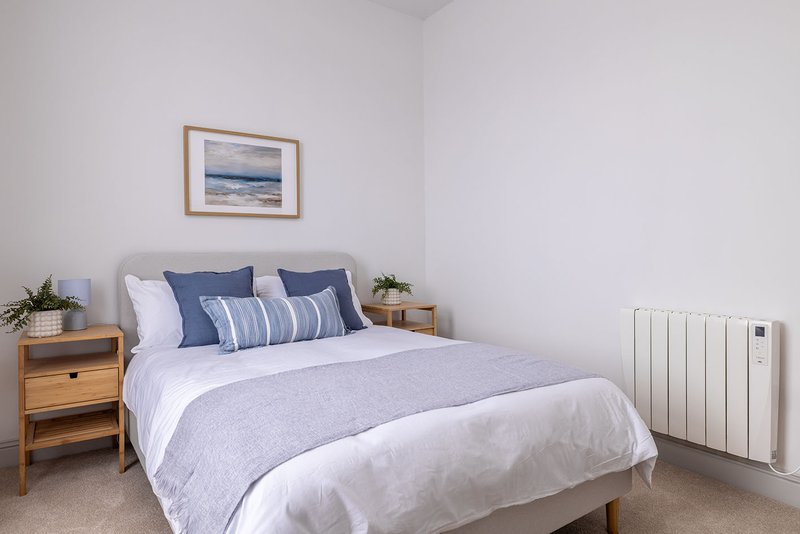 Bright bedroom with double bed, blue bedding, wooden nightstand and white radiator