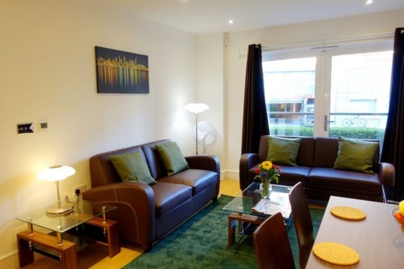 Spacious living room with blue sofa, armchair, glass coffee table and dining area by windows
