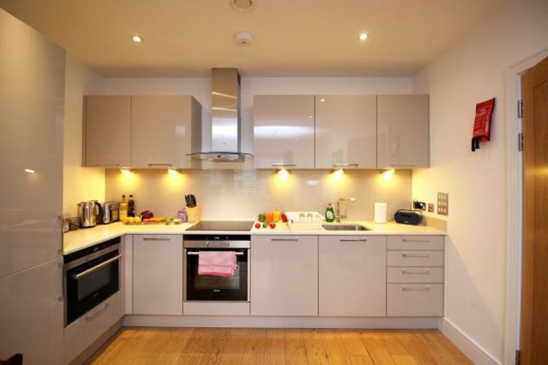 Modern white kitchen with built-in appliances, under-cabinet lighting, and wooden flooring
