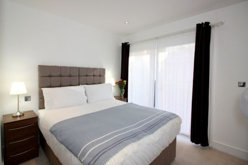 Modern bedroom with double bed, upholstered headboard, bedside table and glass door access