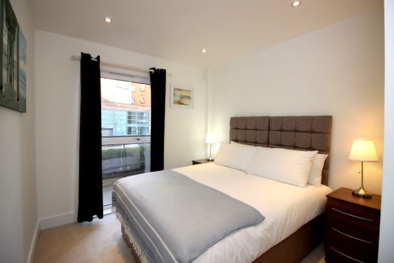 Modern bedroom with double bed, brown headboard, bedside lamp and balcony doors with black curtains