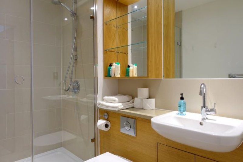Modern bathroom with wooden vanity, white sink, glass shower enclosure and mirror cabinet