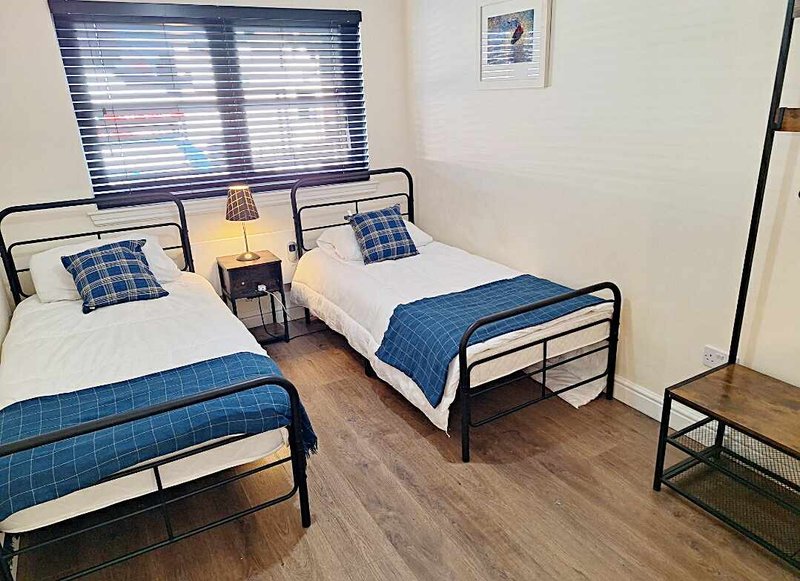 Twin bedroom with two single beds, blue bedding, wooden floor and window blinds