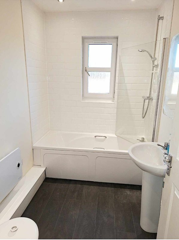 Clean modern bathroom with white subway tile walls, pedestal sink, bathtub and window