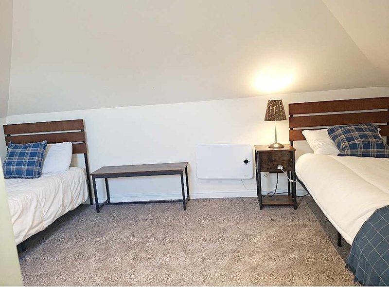 Attic bedroom with two single beds, plaid pillows, carpet flooring and sloped ceiling