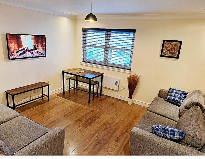 Modern living room with wooden flooring, grey sofas, desk, wall-mounted TV and framed artwork