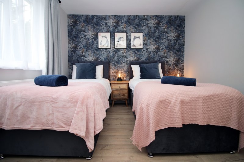 Twin bedroom with pink quilts, navy headboard, framed wall art and bedside lamps