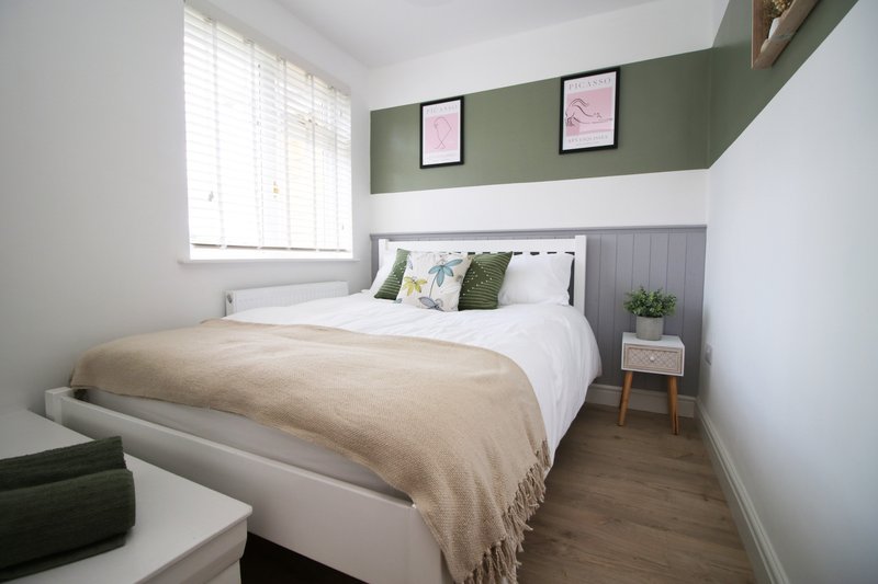 Modern bedroom with double bed, green feature wall, framed artwork, and natural light from window