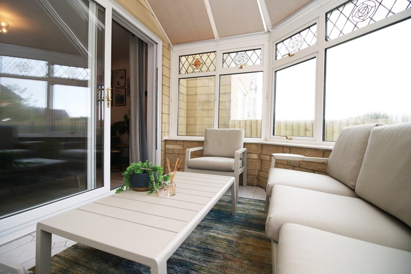 Bright conservatory with cream upholstered seating, white coffee table, potted plant and garden views