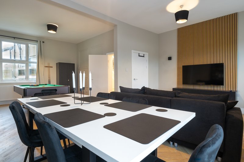 Modern open-plan living room with dining table, black sofa, TV wall and wood paneling