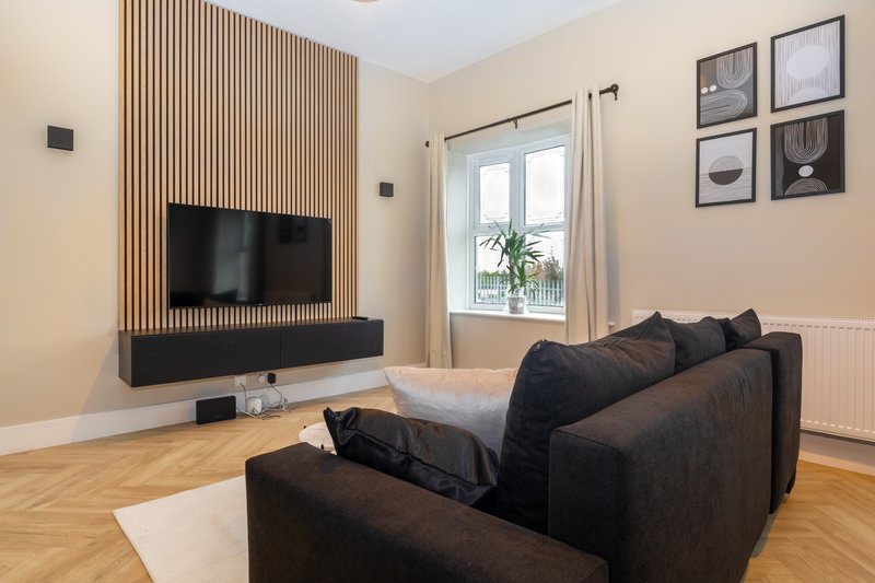 Modern living room with black sofa, wall-mounted TV, wooden floor and large window