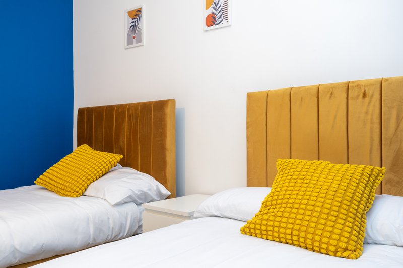 Modern bedroom with two single beds, mustard-yellow cushions, and blue accent wall