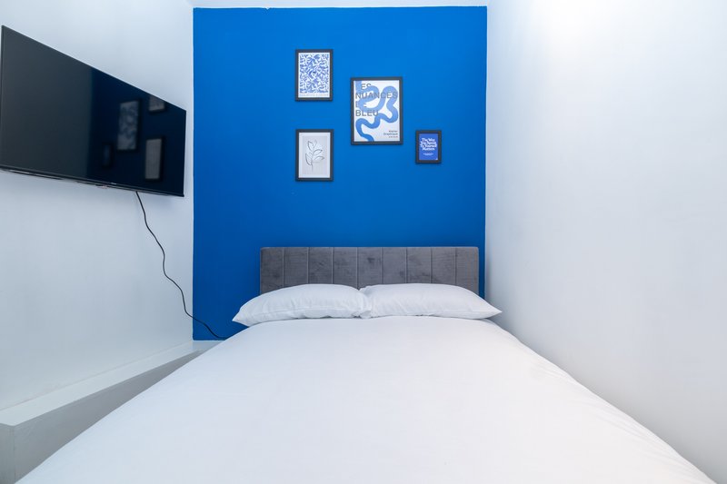 Modern bedroom with double bed, blue accent wall, mounted TV and framed wall art
