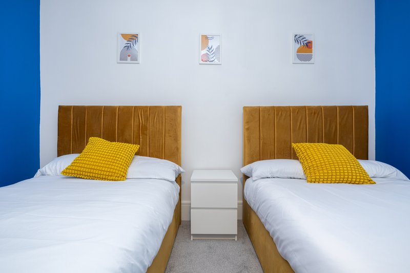 Twin bedroom with wooden headboards, yellow pillows, white bedding and blue accent wall