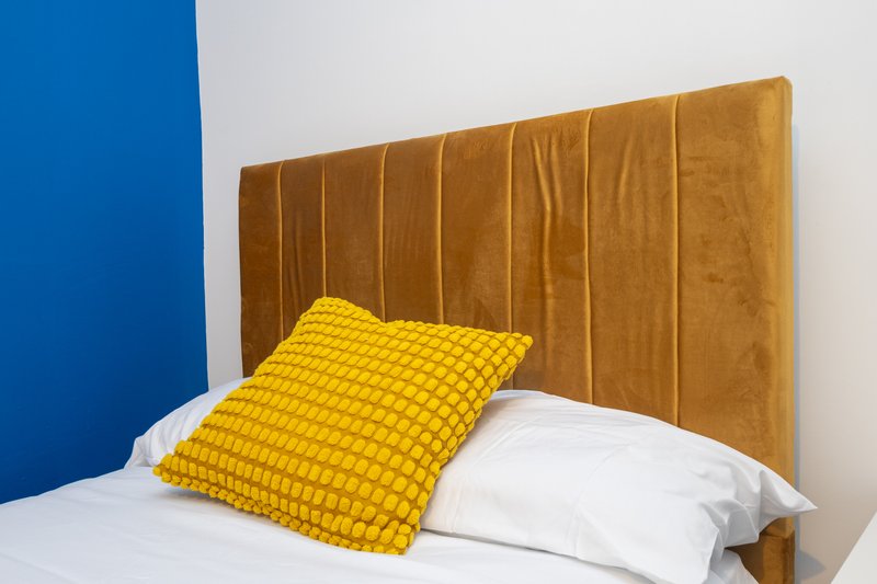 Modern bedroom with golden upholstered headboard, yellow quilted pillow and white bedding