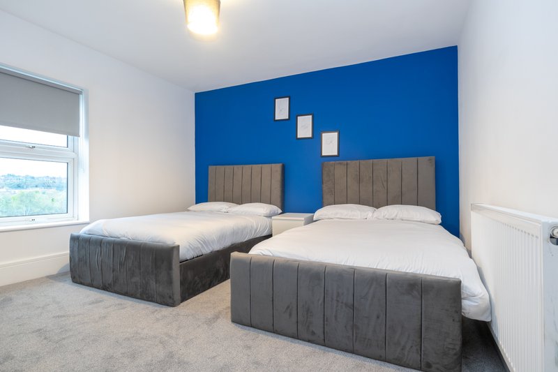 Bright bedroom with two single beds, blue accent wall, and large window with countryside view