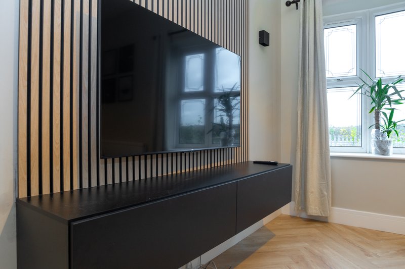Modern living room with wall-mounted TV, black media console, wooden flooring and bright windows