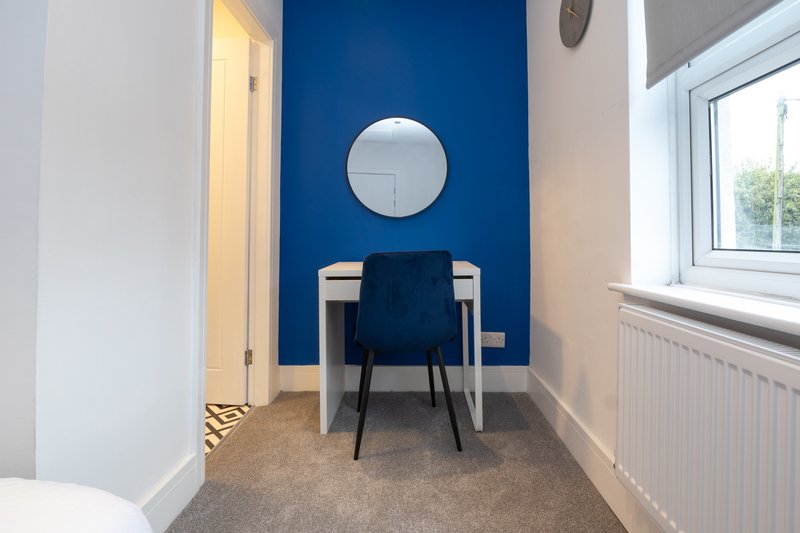 Modern home office with blue accent wall, round mirror, desk chair and window view