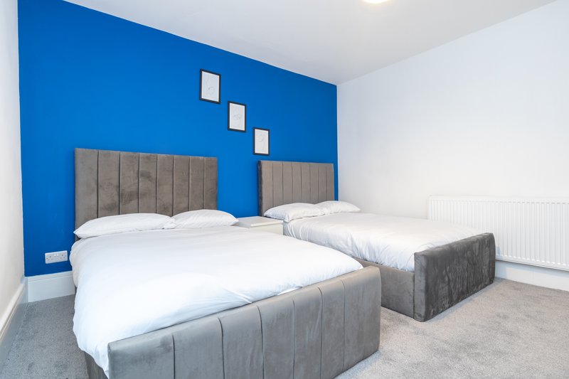 Modern bedroom with two double beds, grey upholstered headboards, white bedding, and bright blue accent wall