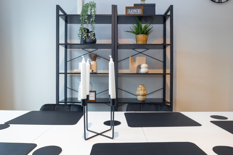 Modern dining table with black and white patterned runner, black metal shelving unit with potted plants and decorative items