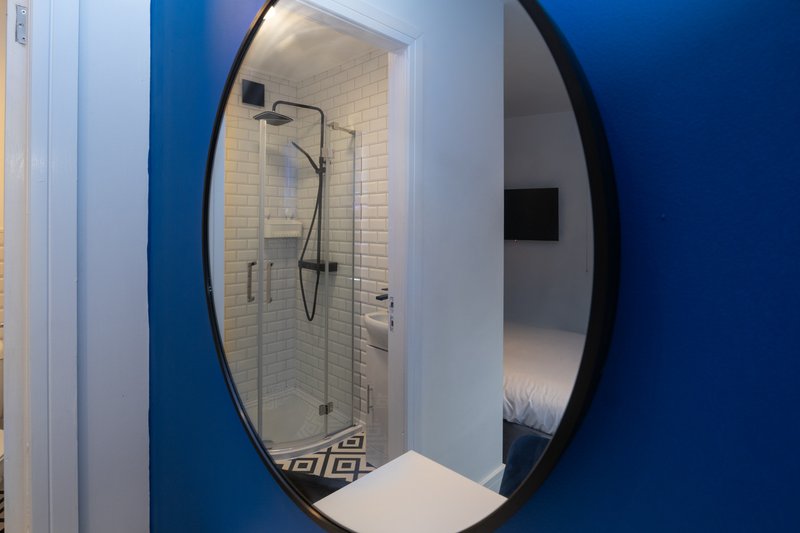 Modern bathroom with large circular mirror, glass shower enclosure and white tile walls