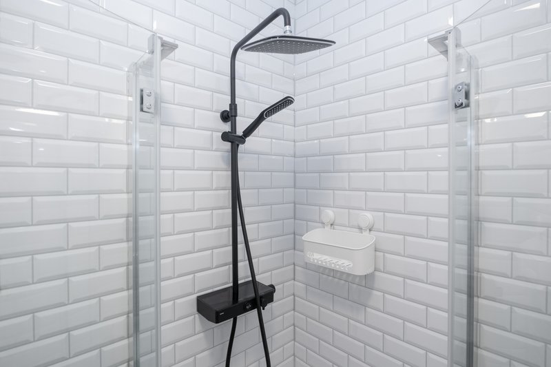 Modern shower enclosure with black rainfall showerhead, white subway tiles and glass doors