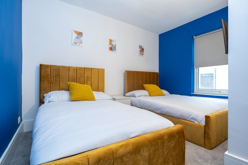 Bedroom with two single beds, wooden headboards, yellow cushions and white bedding