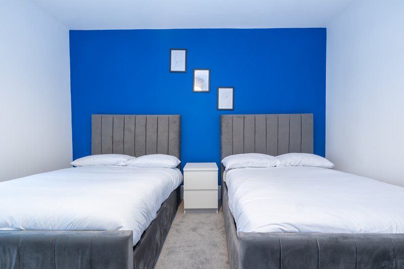 Modern twin bedroom with grey upholstered headboards, white bedding, and bright blue accent wall