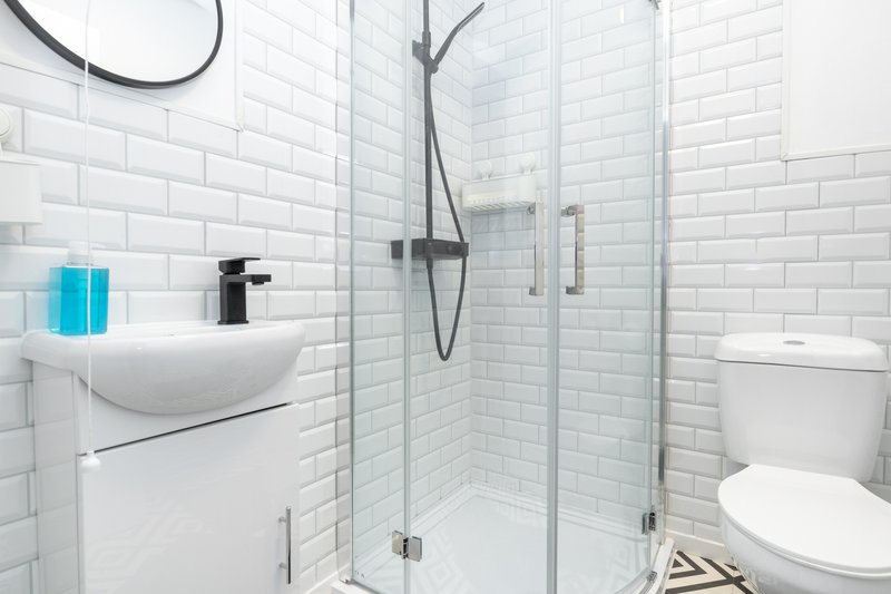 Modern white-tiled bathroom with sink, shower enclosure, toilet and toiletries