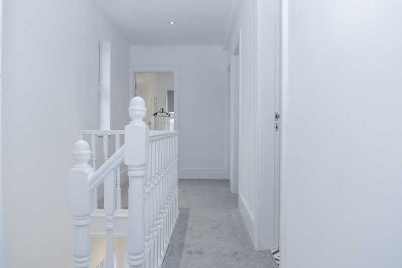 Bright hallway with white staircase railing, wooden handrail, and grey carpet flooring