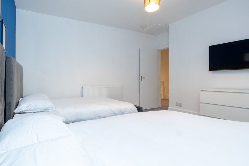 Modern bedroom with two single beds, white bedding, wall-mounted TV and wooden door