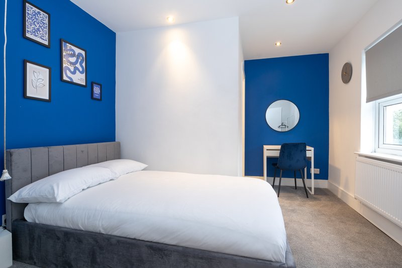 Modern bedroom with double bed, blue accent wall, framed artwork and desk area