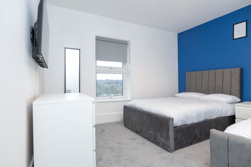 Modern bedroom with double bed, blue accent wall, window and contemporary furnishings