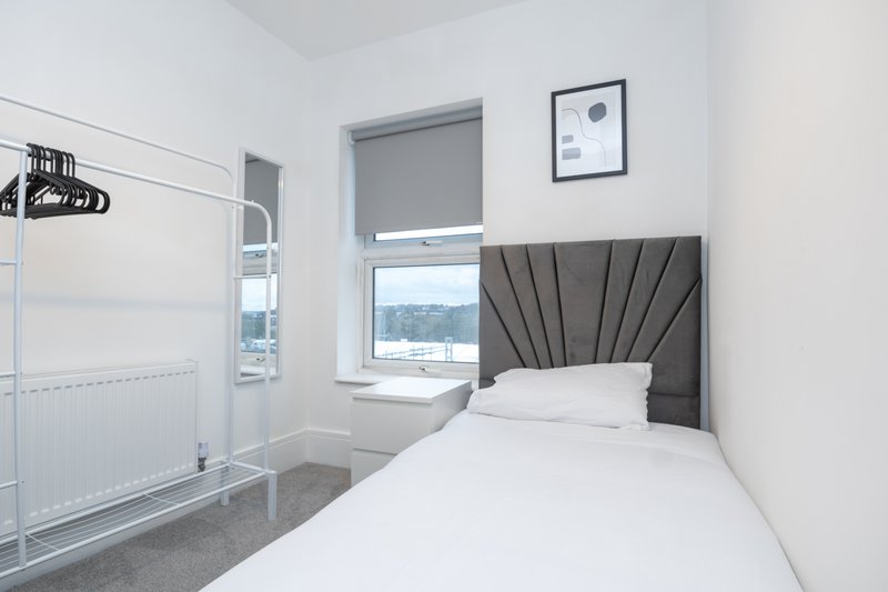 Bright bedroom with single bed, grey headboard, window view and modern furnishings