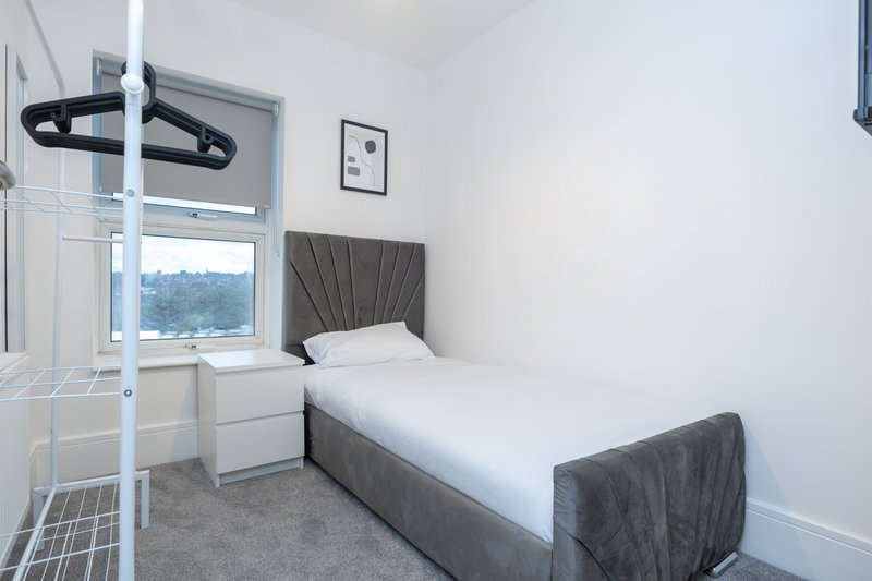 Bright modern bedroom with single bed, grey headboard, white walls and window view