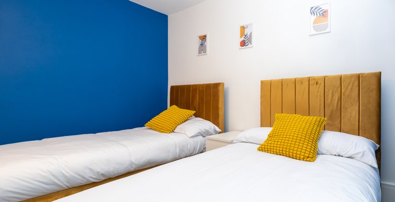 Twin bedroom with yellow headboards, white bedding, yellow cushions and blue accent wall